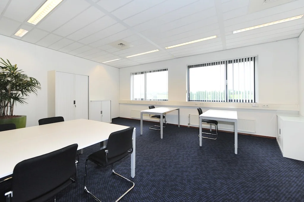 Licht en modern kantoor aan de Laan van S-Gravenmade met witte bureaus, zwarte stoelen en grote ramen met verticale lamellen.